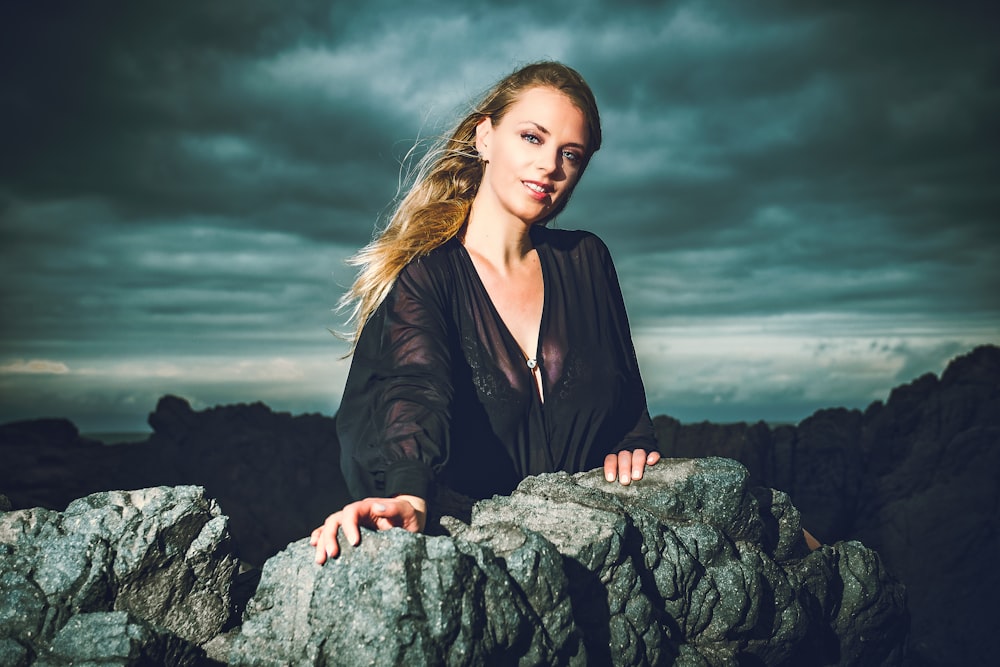 woman in black blazer sitting on gray rock