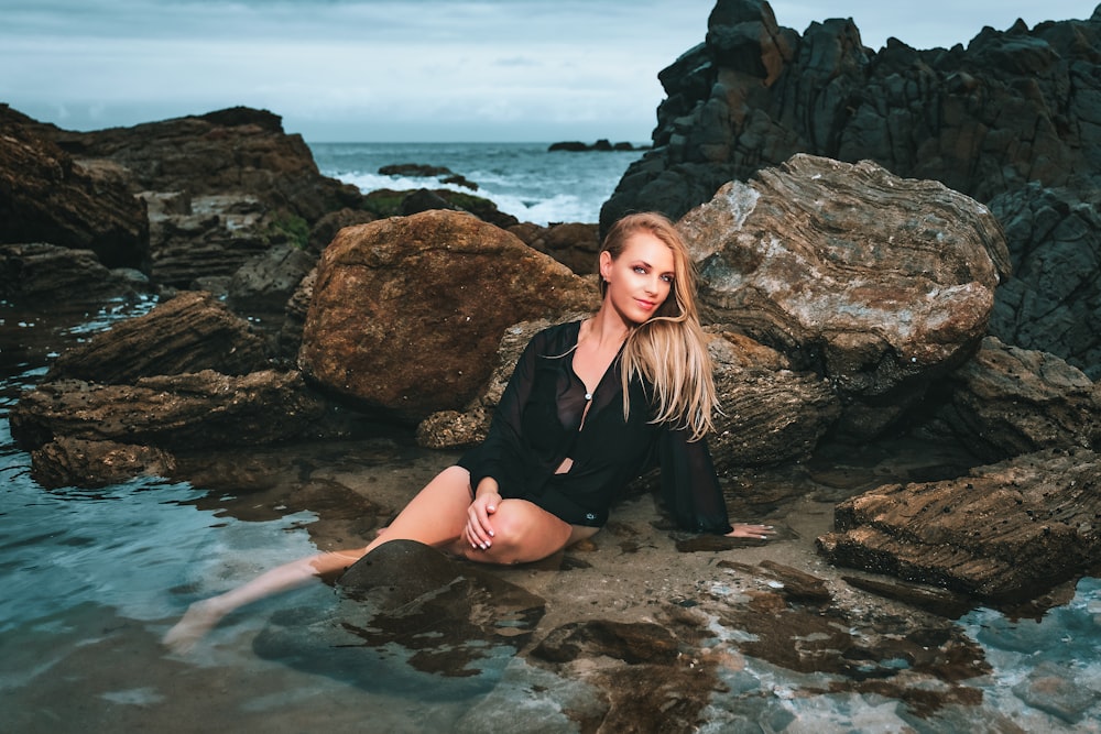 femme en robe noire assise sur le rocher dans l’eau