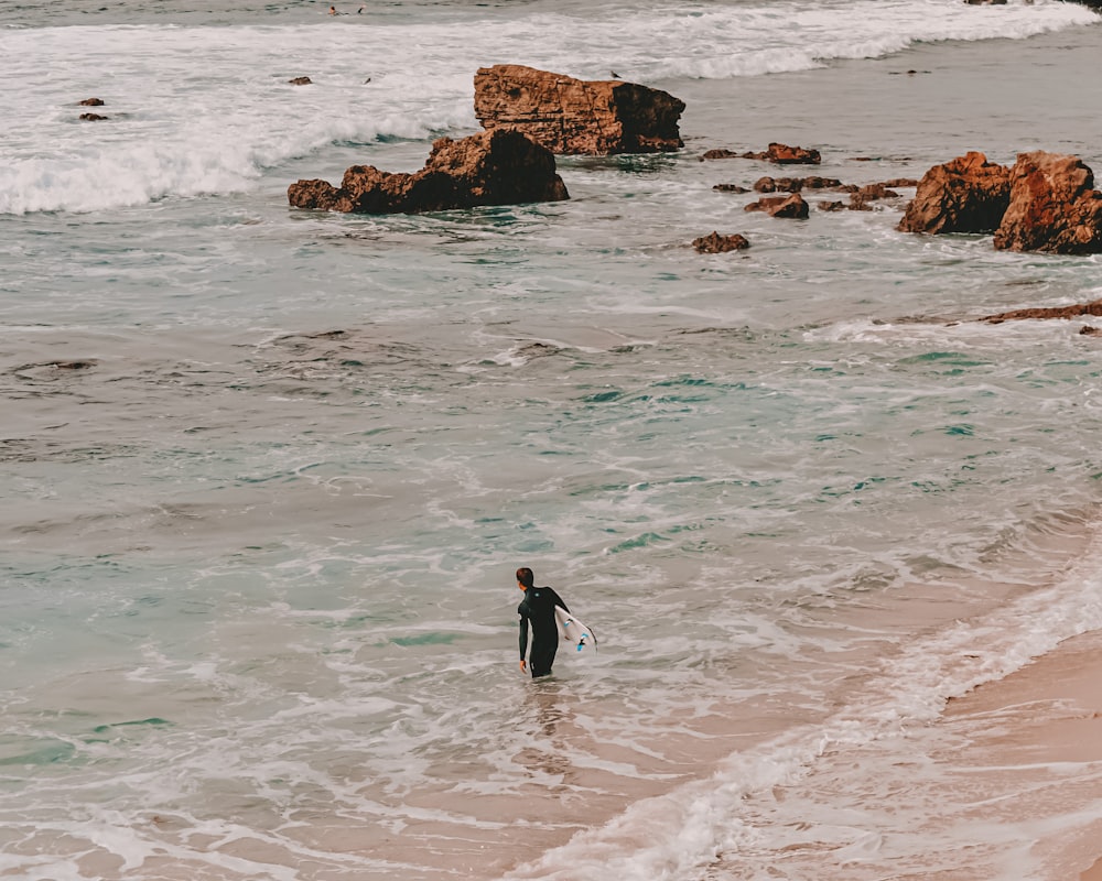 man in black wet suit walking on beach shore during daytime