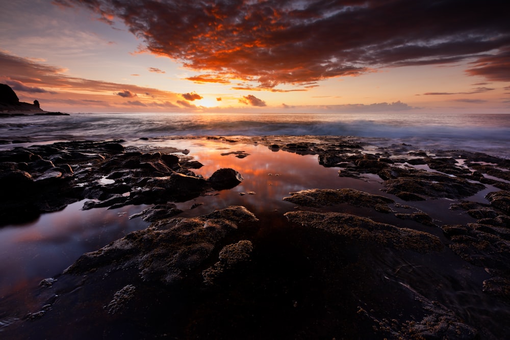 rocky shore under orange and blue cloudy sky during sunset