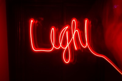 Red neon light creates a handwritten-style word against a dark background, producing a vibrant and lively effect.