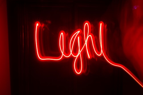 Red neon light creates a handwritten-style word against a dark background, producing a vibrant and lively effect.