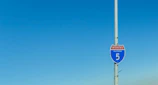 Traffic control signs and barriers set up along a busy California road under clear skies.