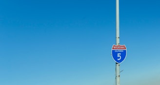 A California Interstate 5 road sign attached to a tall pole with a clear blue sky in the background.