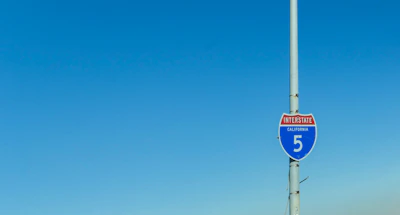 Traffic control signs and barriers set up along a busy California road under clear skies.
