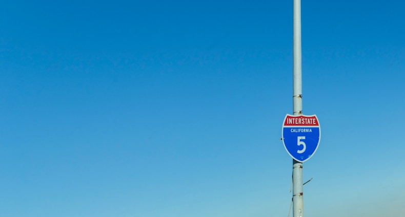 A California Interstate 5 road sign attached to a tall pole with a clear blue sky in the background.