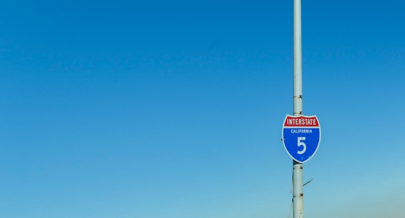 A California Interstate 5 road sign attached to a tall pole with a clear blue sky in the background.