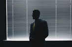 man in black suit standing near window blinds