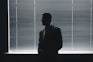 man in black suit standing near window blinds