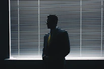 man in black suit standing near window blinds