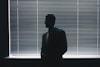 man in black suit standing near window blinds