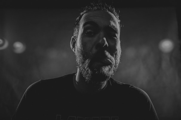 A vintage-style black and white photo of a man applying beard oil, captured mid-motion with soft natural light.