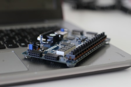 A microcontroller or prototyping board is placed on top of a partially visible laptop keyboard. The board has various components like resistors, capacitors, and a digital display.