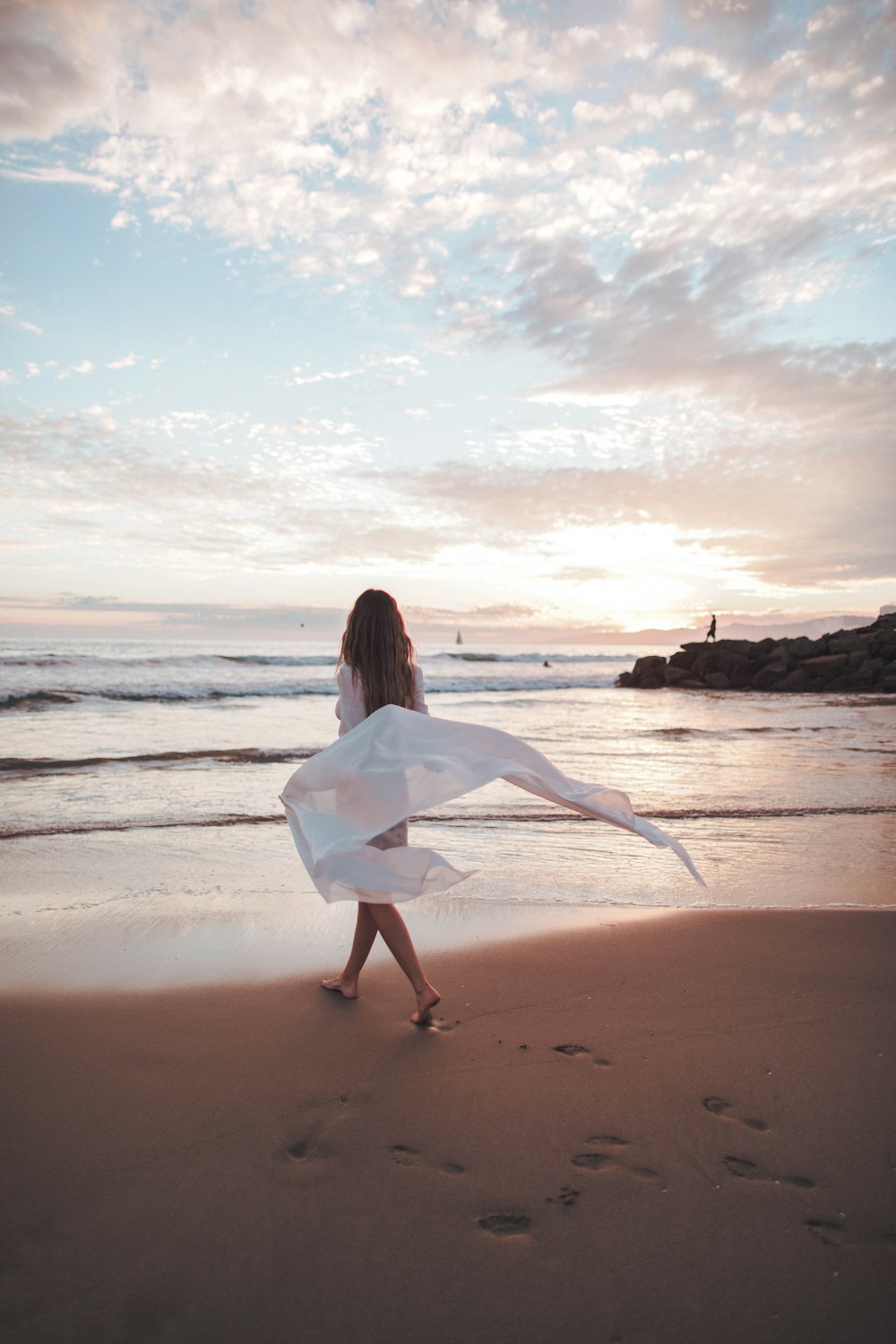 昼間のビーチを歩く白いドレスの女性