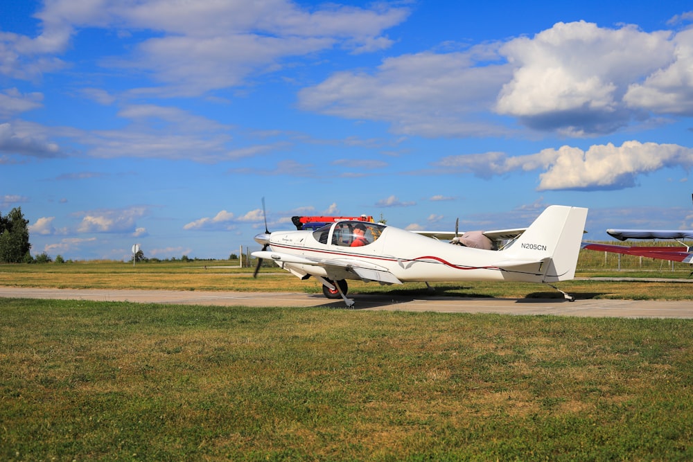 white and red airplane on green grass field under blue sky and white clouds during daytime