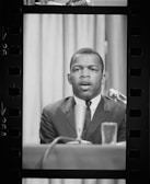 A serious male politician speaking at a podium with blue lighting.