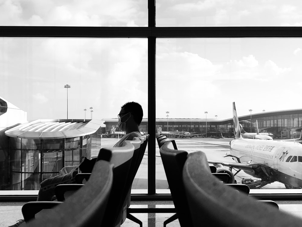 grayscale photo of man sitting on chair near window