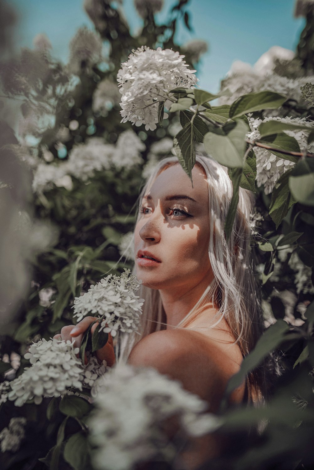 woman in white floral lace top standing beside green plant