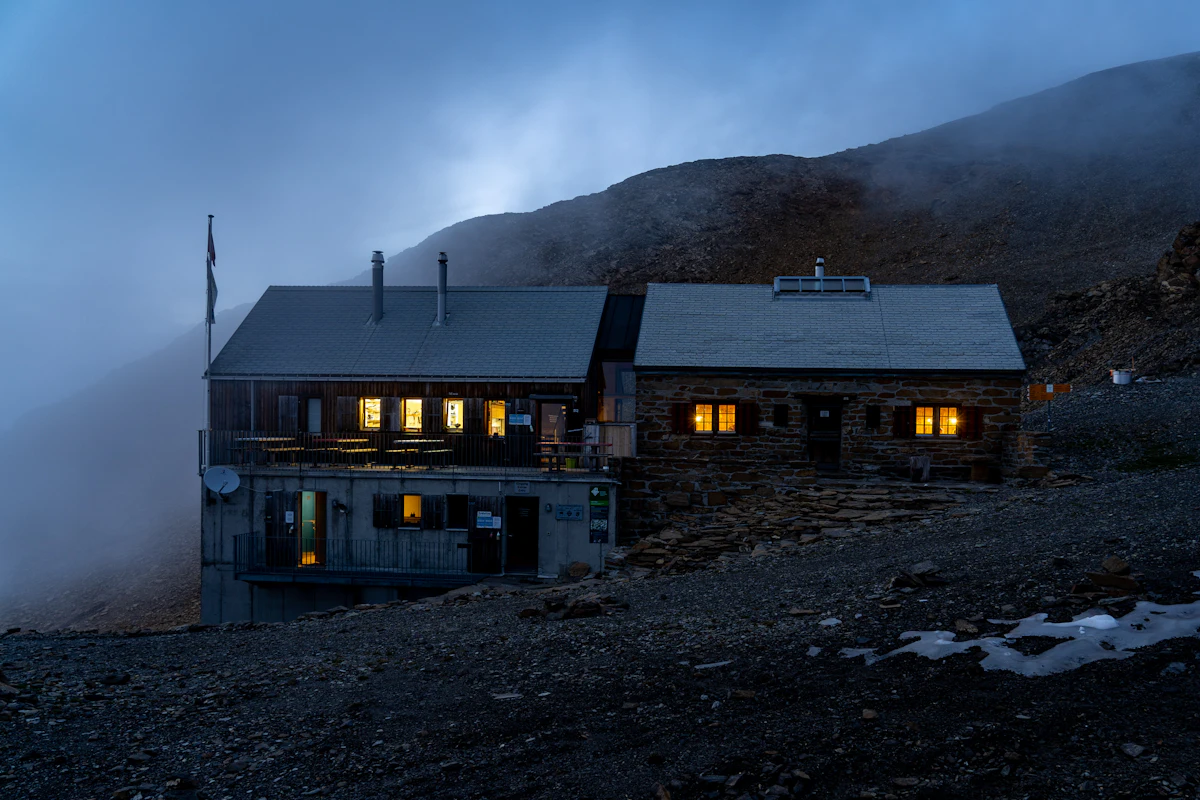 The Wildstrubel hut at dusk, its windows lit, on a stony slope in low cloud