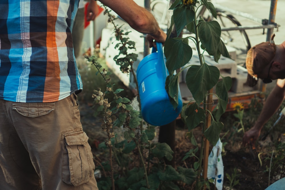 man in orange and white stripe shirt and brown cargo pants holding blue plastic container