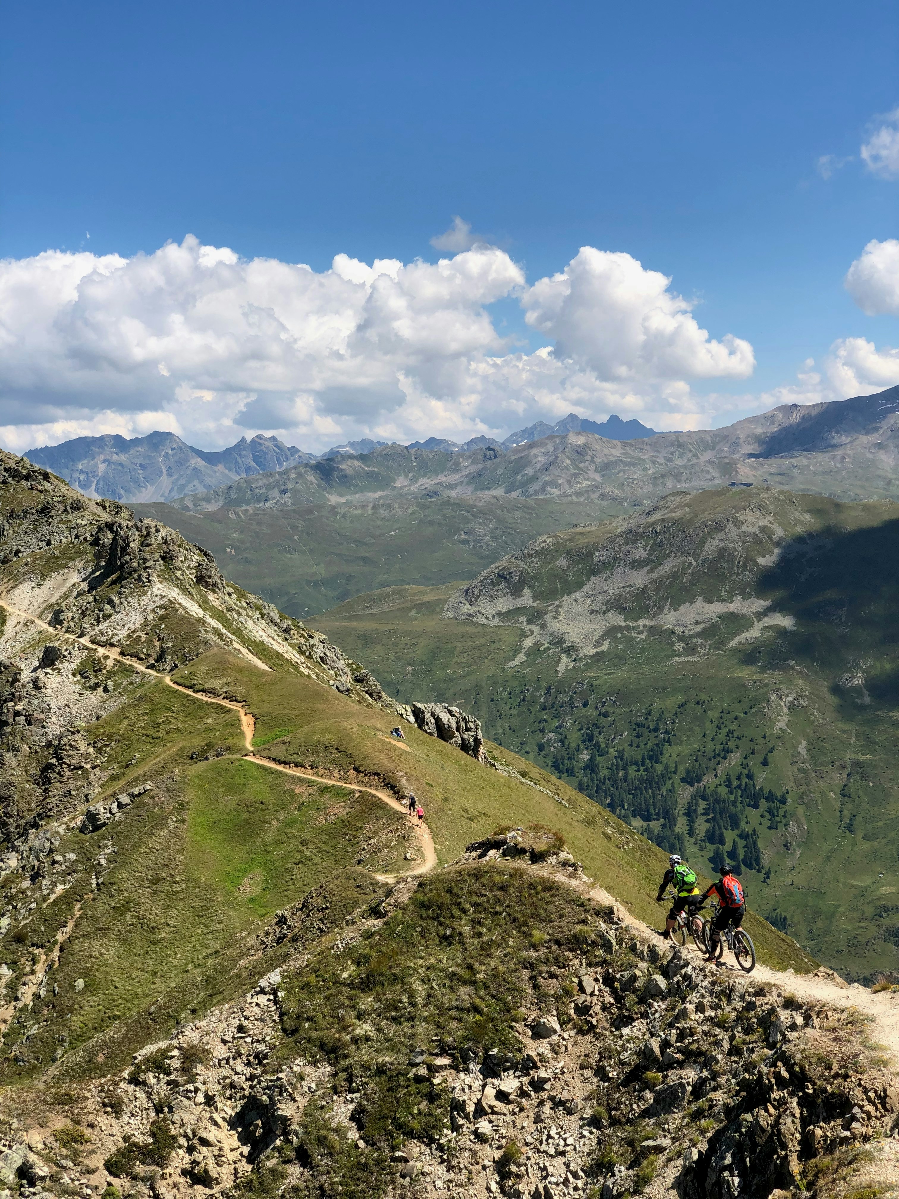 people hiking on green mountain under white clouds and blue sky during daytime