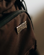 A close-up view of a brown fabric material featuring a patch with the word 'BRAVOS' sewn onto it. The texture of the fabric is visible, highlighting its woven pattern, and the patch stands out due to its metallic sheen.