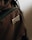 A close-up view of a brown fabric material featuring a patch with the word 'BRAVOS' sewn onto it. The texture of the fabric is visible, highlighting its woven pattern, and the patch stands out due to its metallic sheen.