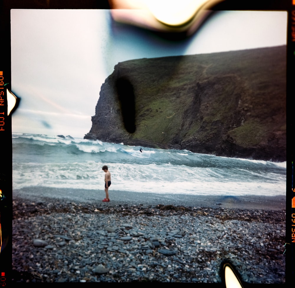 Persona con pantalones negros de pie en la costa rocosa gris durante el día