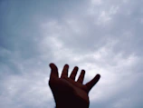 Hands reaching upward from darkness toward a radiant light breaking through clouds.