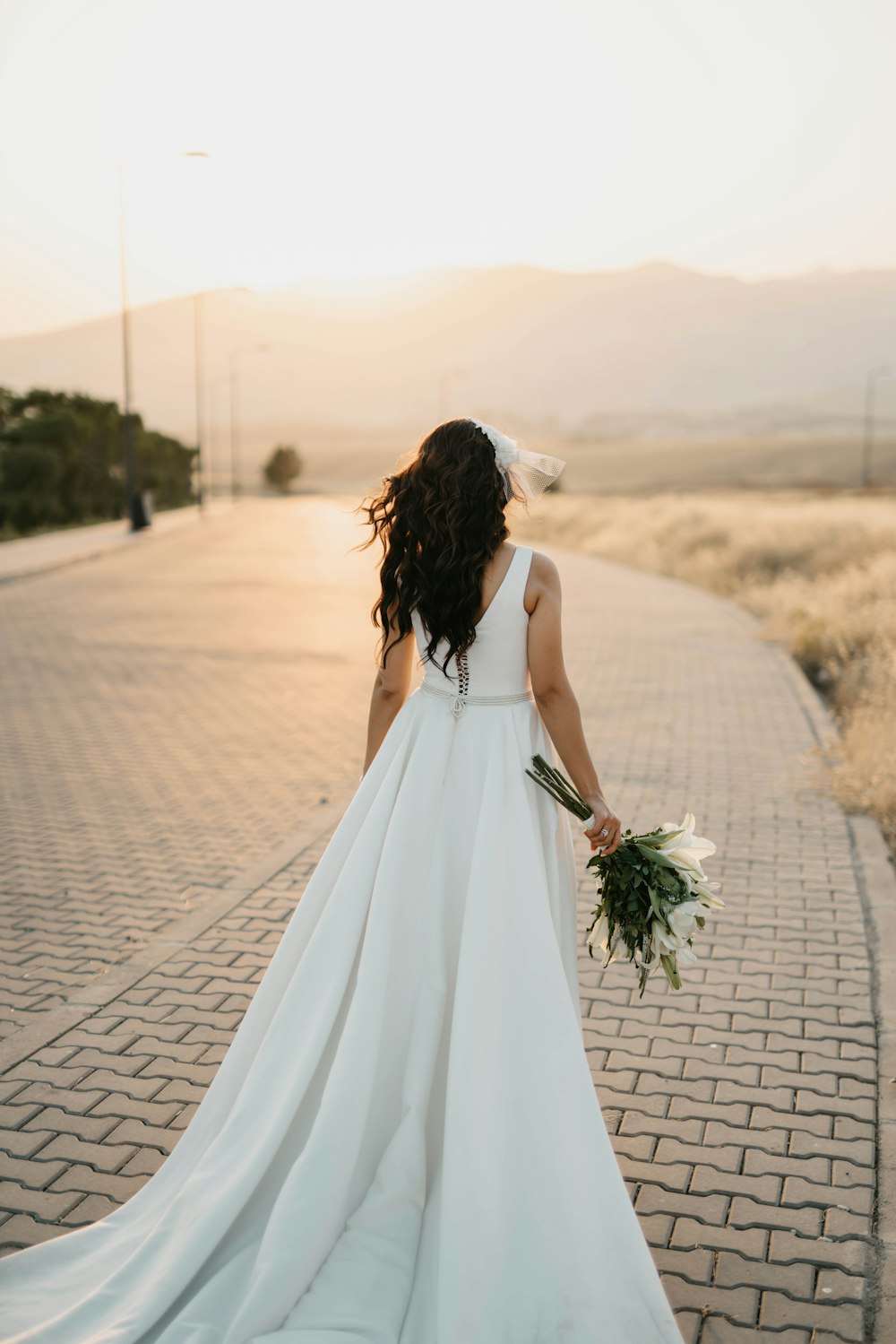 woman in white tube dress holding bouquet of flowers walking on pathway during daytime
