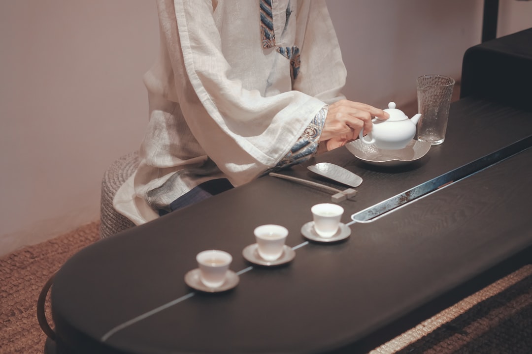 person in white robe holding white ceramic teacup on saucer
