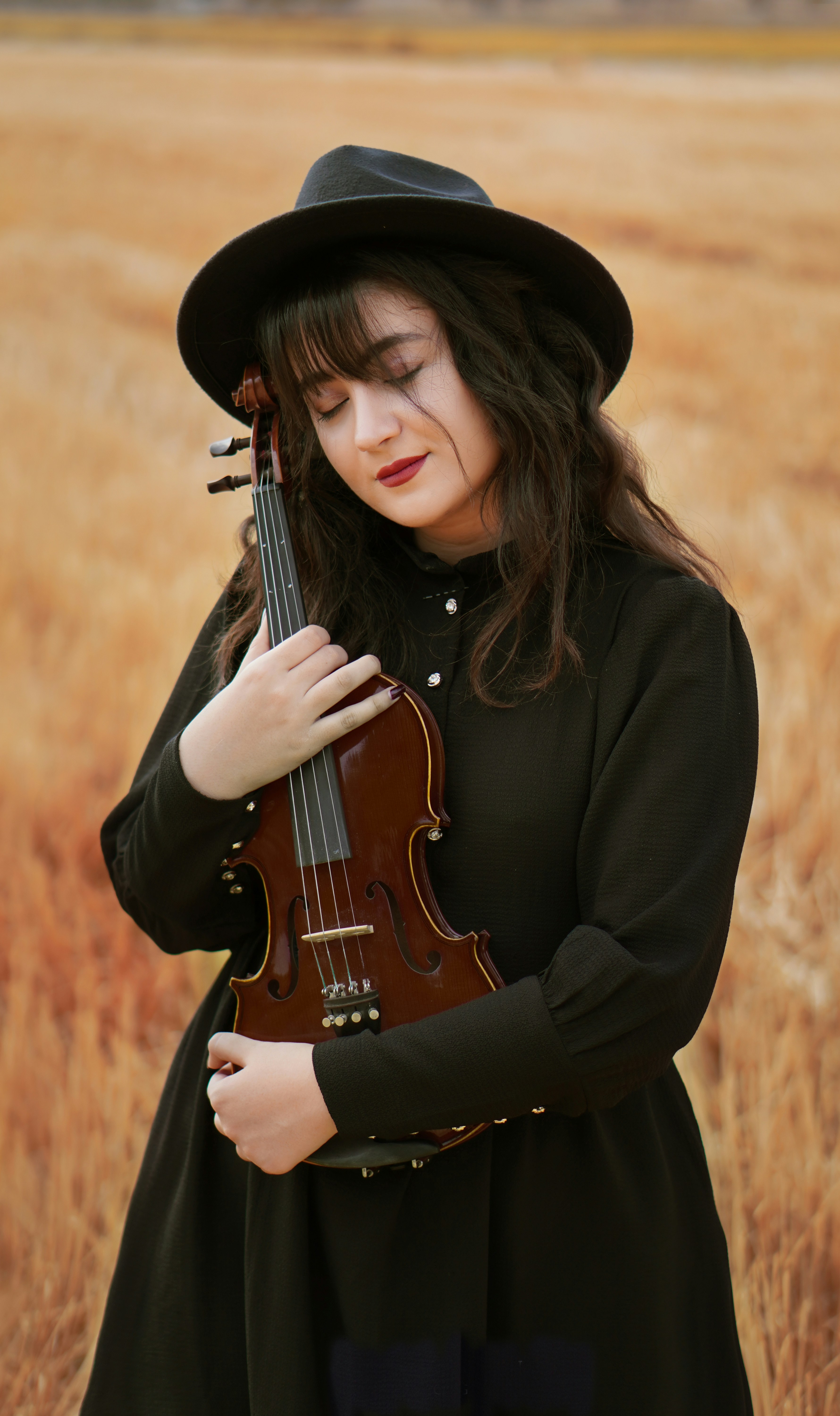 Mujer con camisa negra de manga larga sosteniendo un violín marrón