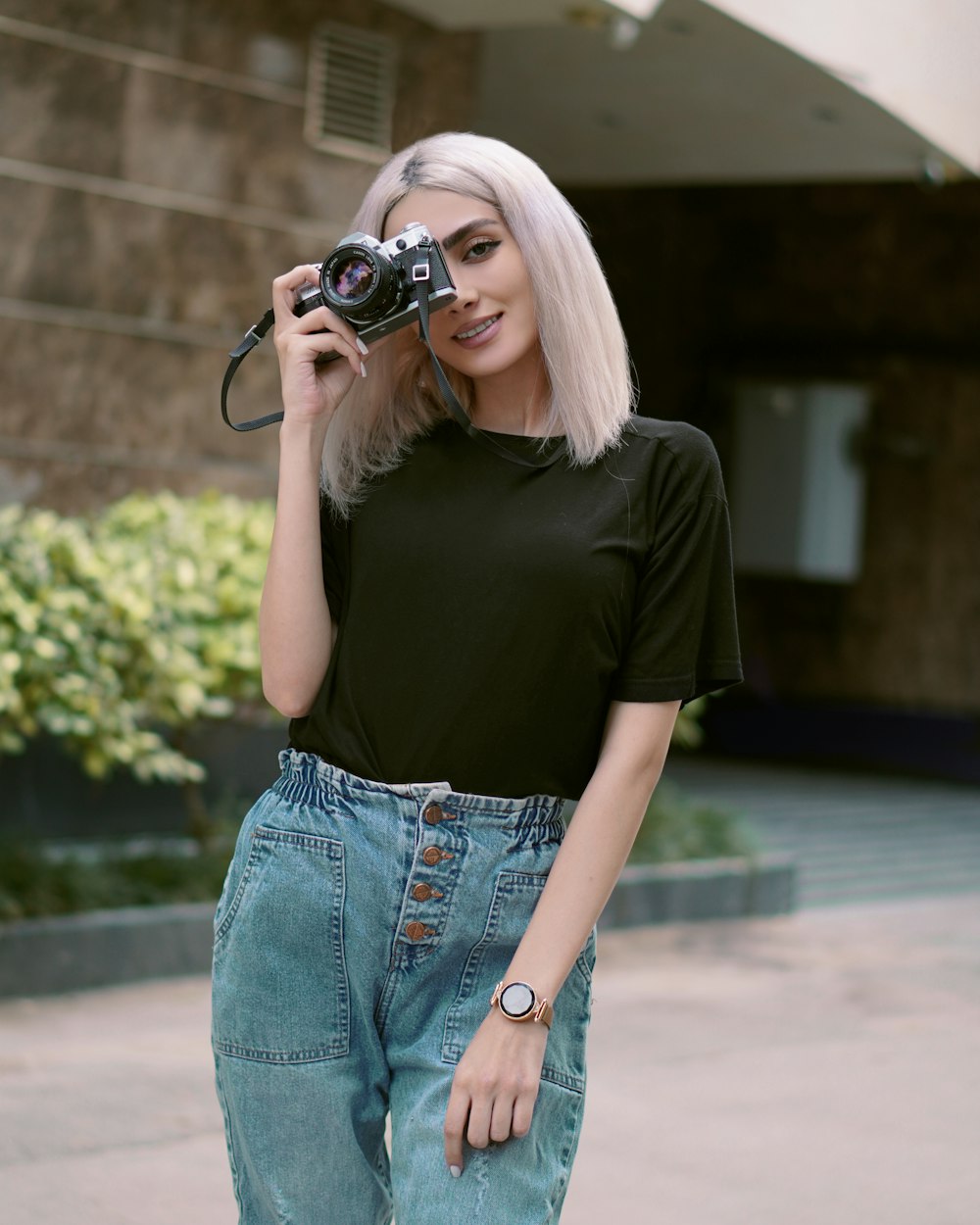 Frau in schwarzem T-Shirt und blauer Jeans mit schwarzer DSLR-Kamera