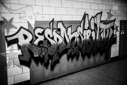 Graffiti art featuring the word 'RESPONSIBILITY' painted in a bold, stylized font across a series of lockers. The background consists of tiled walls, and there are star motifs incorporated into the design. The image is in black and white.