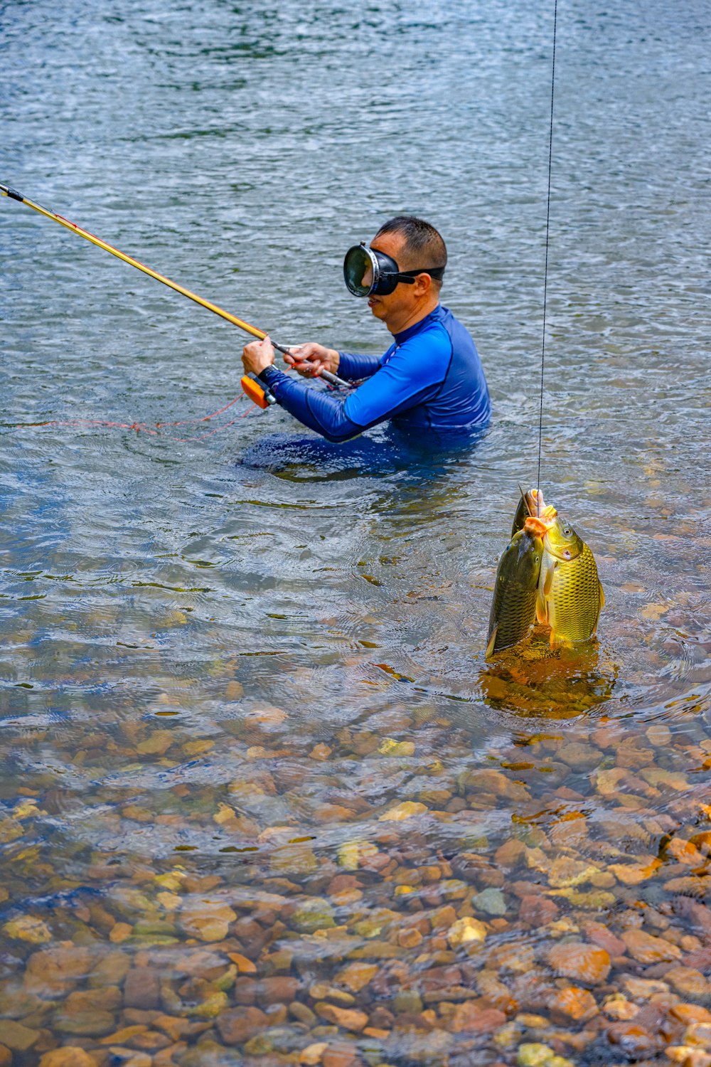 man in blue jacket and blue pants holding fishing rod with fish on water