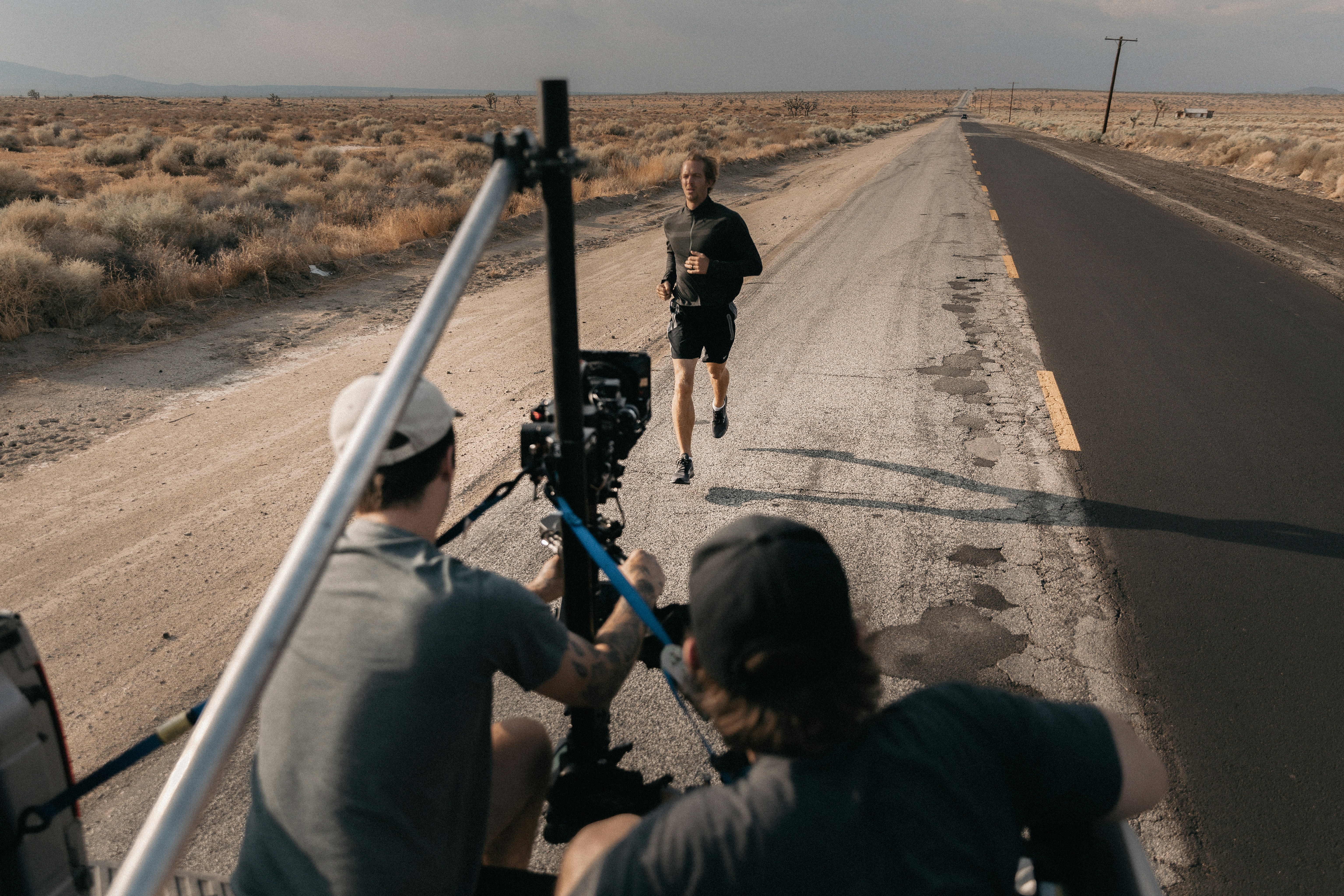A crew films a man running along a desert road, creating content which will use royalty free fitness music.
