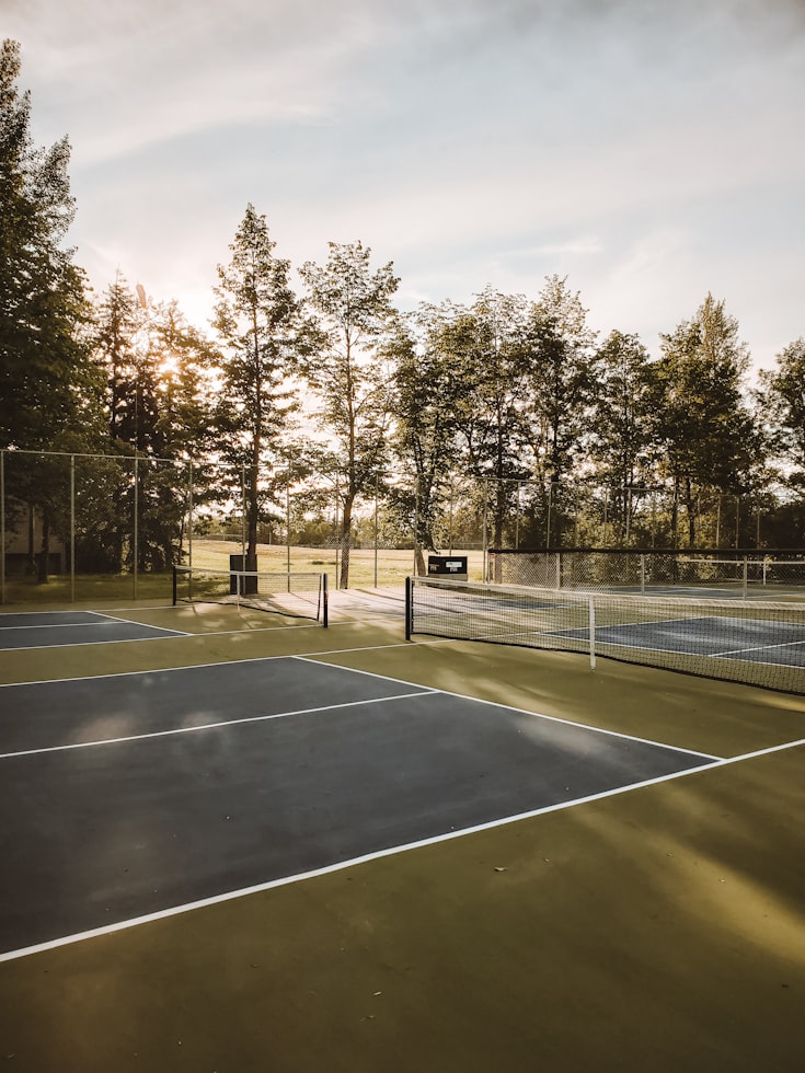 A modern tennis facility with multiple courts stretching into the distance under a blue sky with scattered clouds