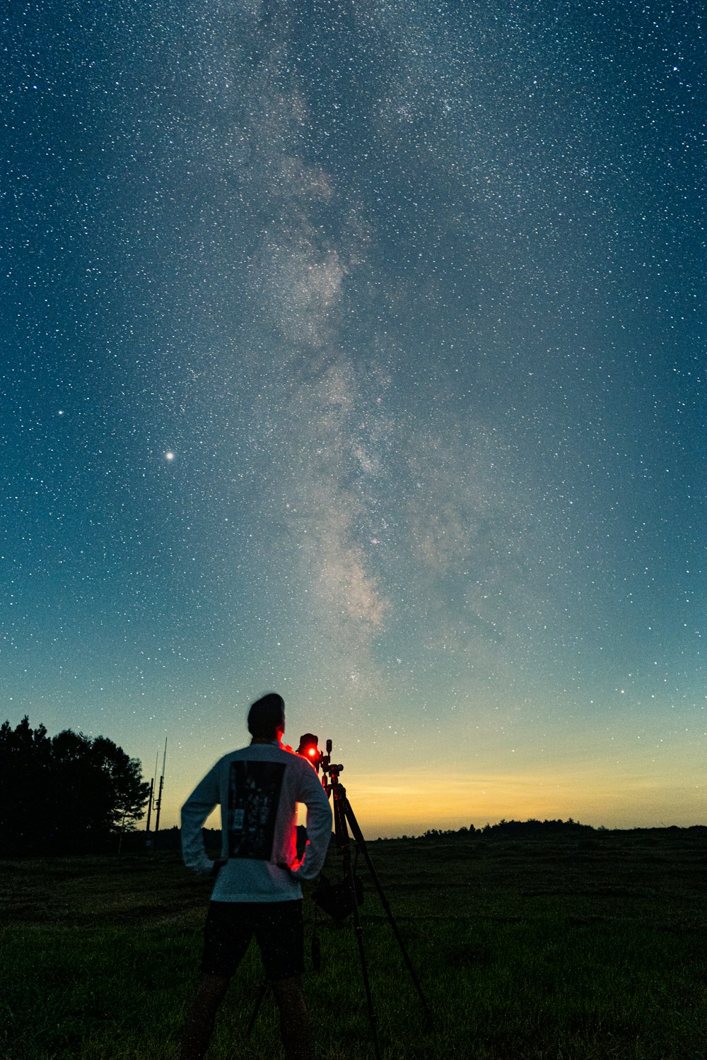 星空の夜の草原に立つ赤いシャツと黒いリュックサックの男