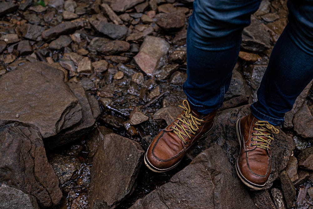 person in blue denim jeans and brown leather shoes standing on rocky ground