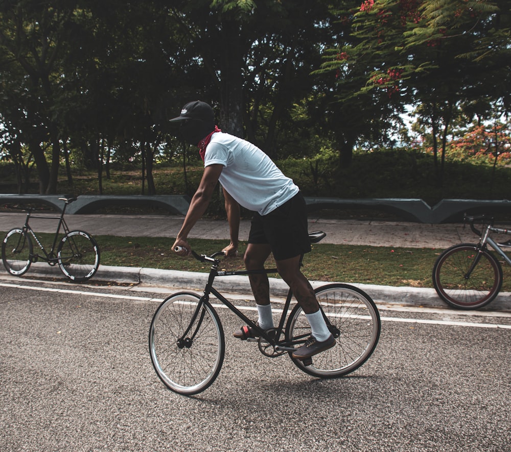 homem na camiseta branca que anda na bicicleta preta na estrada durante o dia