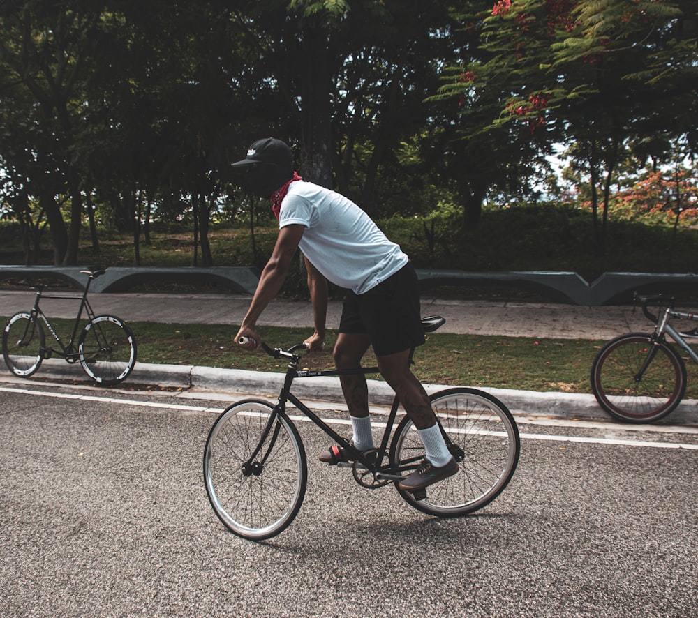 man in white t-shirt riding on black bicycle on road during daytime