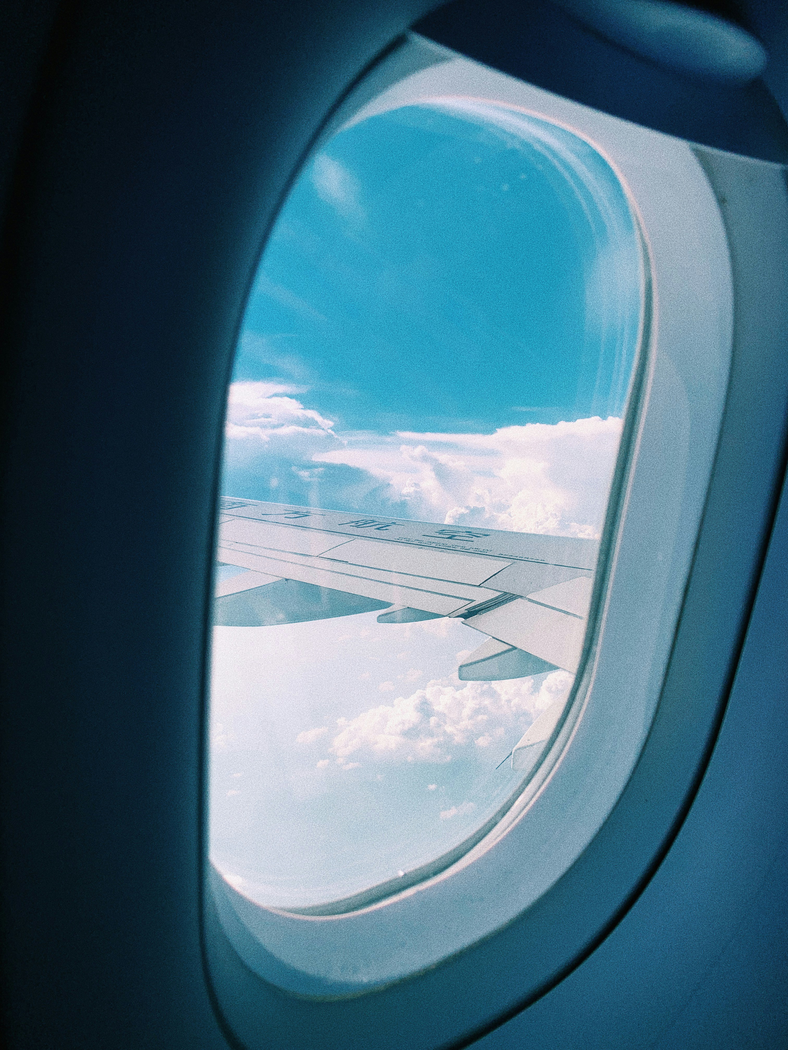 Airplane wing visible through window with clouds below during flight