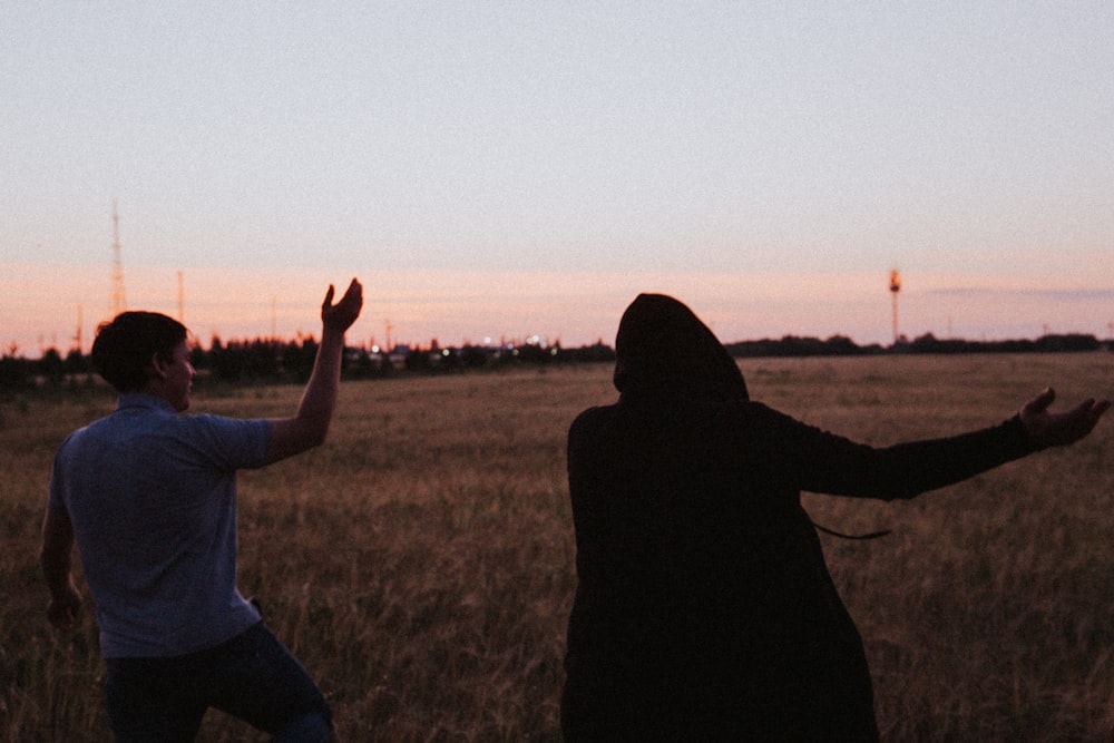 silhouette of 2 person standing on grass field during sunset