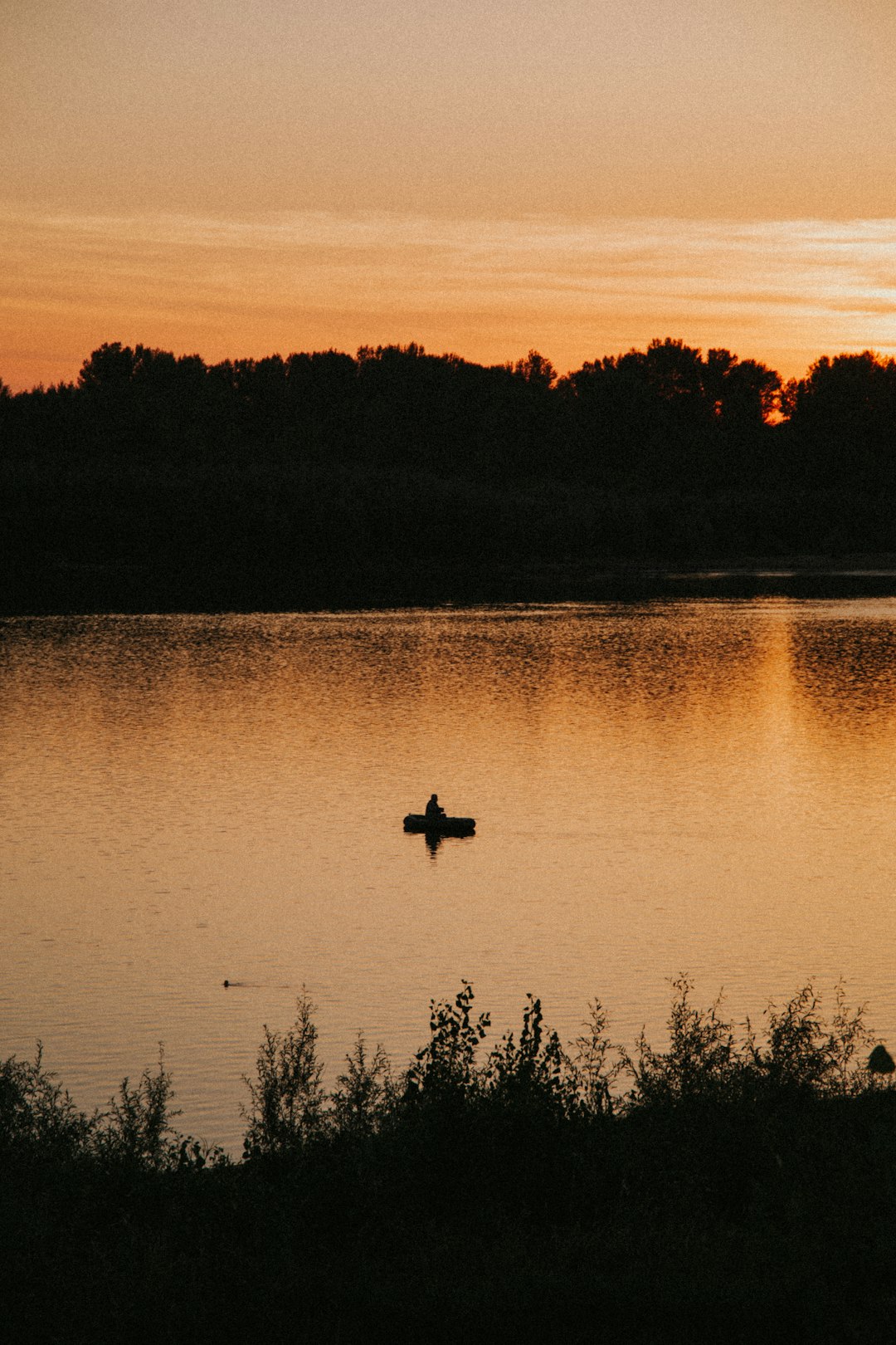 silhouette of man riding on boat on lake during sunset