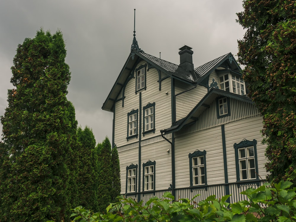 Weißes und schwarzes Haus in der Nähe grüner Bäume unter weißen Wolken während des Tages