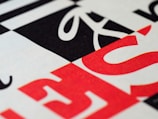Geometric pattern with bold typography featuring overlapping black, white, and red letters. The design includes diagonal and horizontal lines creating a modern and abstract visual.