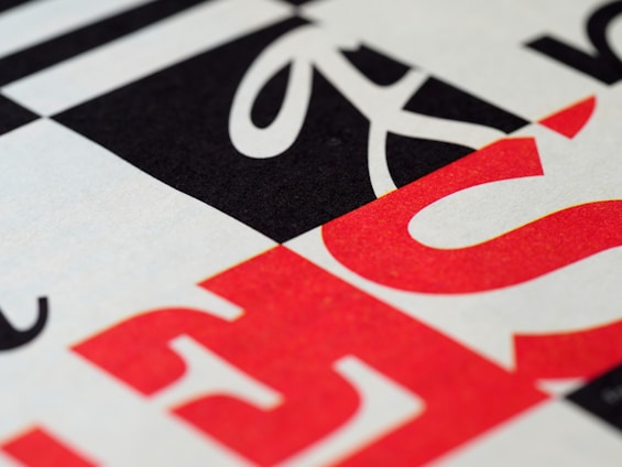 Geometric pattern with bold typography featuring overlapping black, white, and red letters. The design includes diagonal and horizontal lines creating a modern and abstract visual.