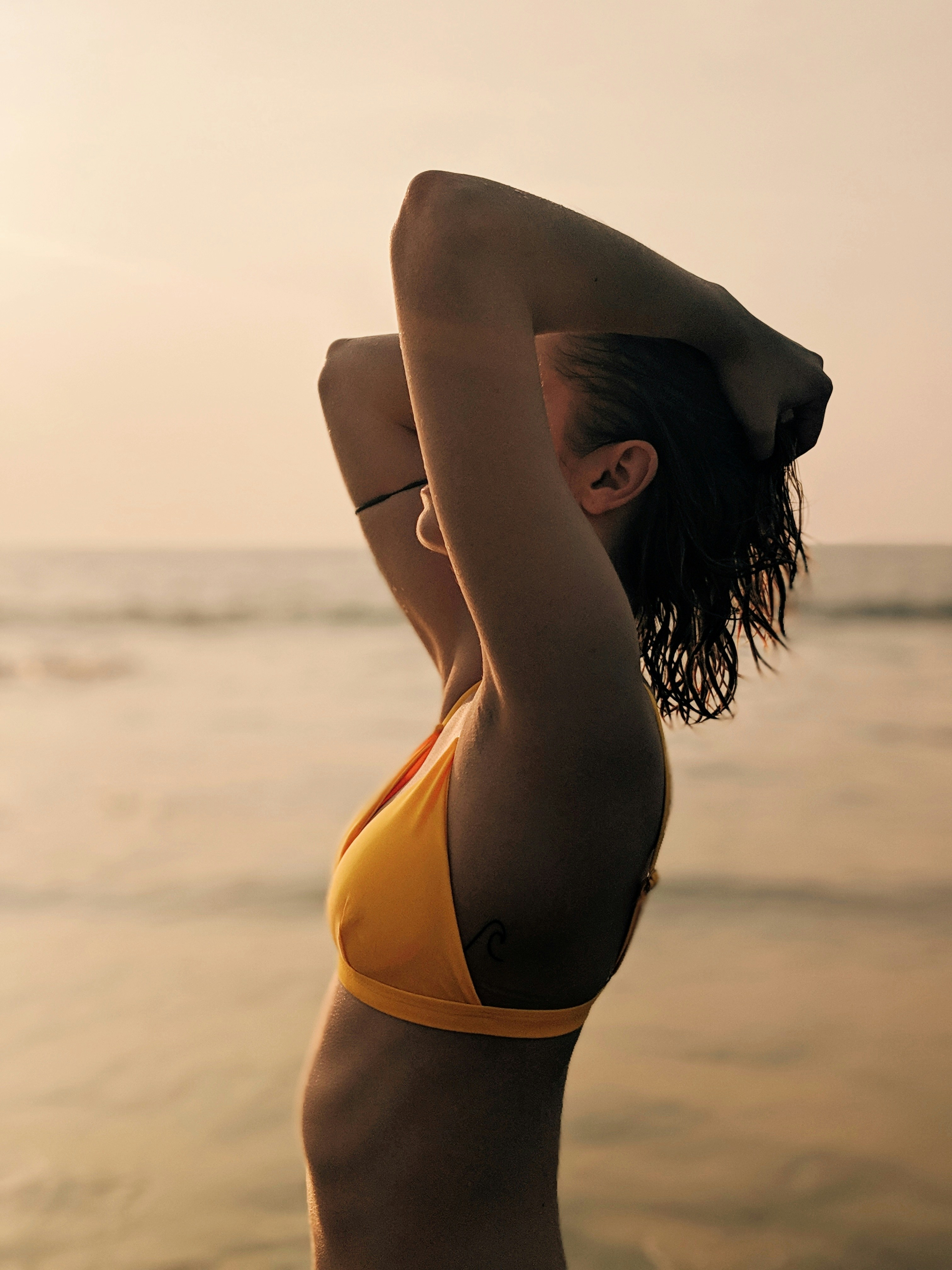 woman in yellow bikini kneeling on beach shore during daytime
