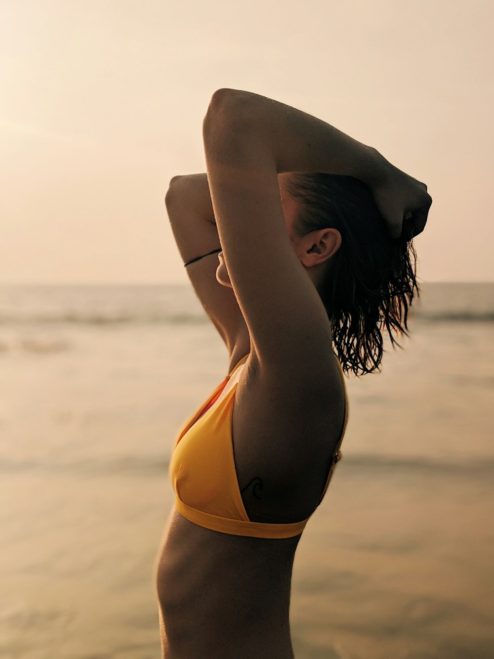 woman in yellow bikini kneeling on beach shore during daytime