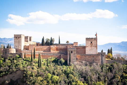 brown concrete building surrounded by green trees under blue sky during daytime in Alhambra Palace Spain